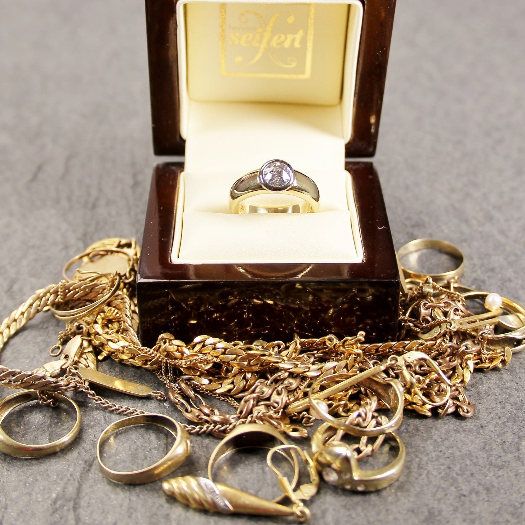 Ein Goldring liegt in seiner Verpackung, umgeben von Goldketten