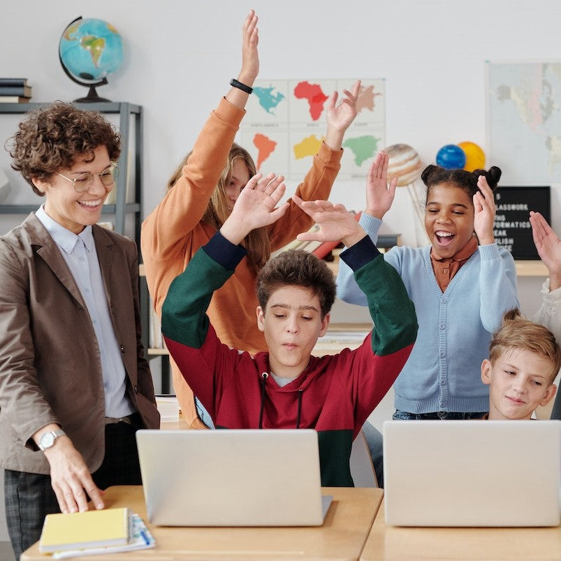 Schulkinder und eine Lehrerin jubeln vor zwei Laptops