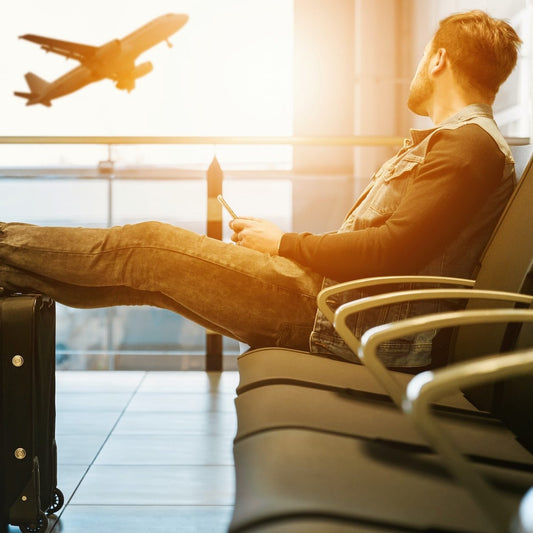 Ein Mann blickt aus dem Fenster eines Flughafen-Gates auf ein fliegendes Flugzeug