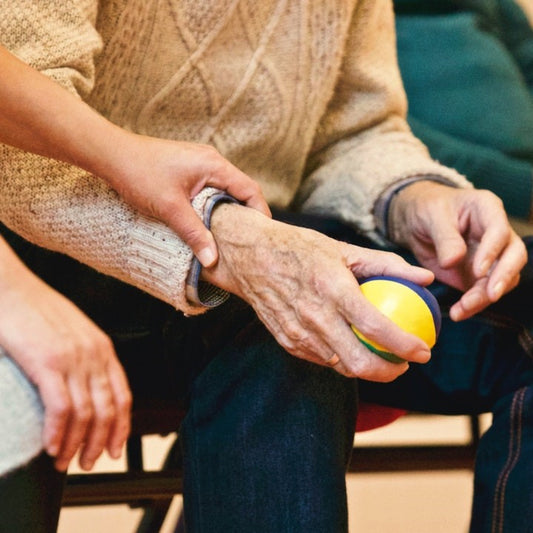 Eine Frau hält den Arm einer sitzenden Seniorin, die einen Ball in der Hand hält