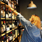 Frau zeigt auf eine Weinflasche in einem Spirituosenladen-Regal